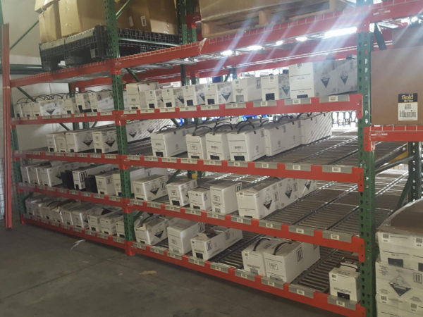 Carton flow rack that's slanted towards the front with a lip to prevent products from falling, filled with batteries in a warehouse.