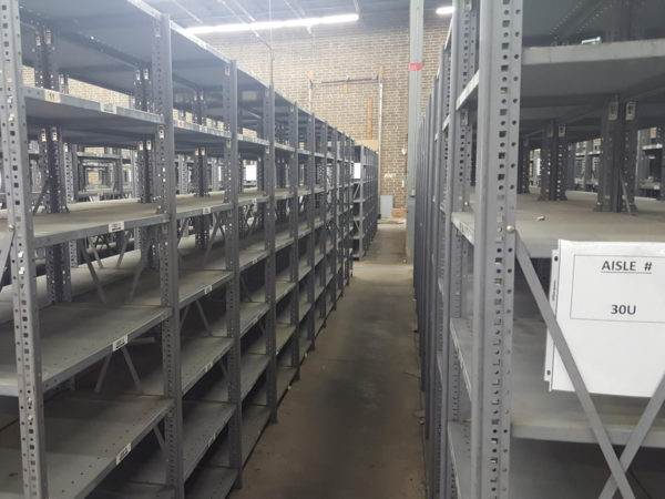 Empty gray metal shelving with aisle numbers in a warehouse.