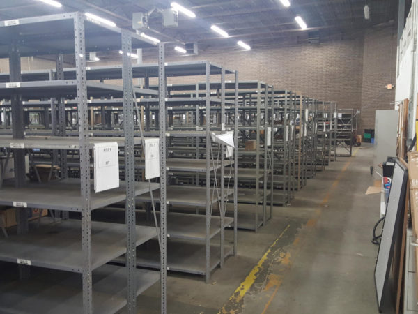 Mostly empty gray metal shelving with aisle numbers in a warehouse.