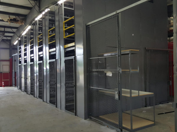 A workbench behind a wire partition, leading to gray metal shelving separated by wire partitions and using a mezzanine to increase storage.