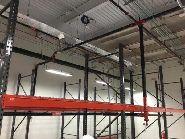 Pallet rack integrated with fire sprinklers, with black uprights, orange beams, and wire decking.