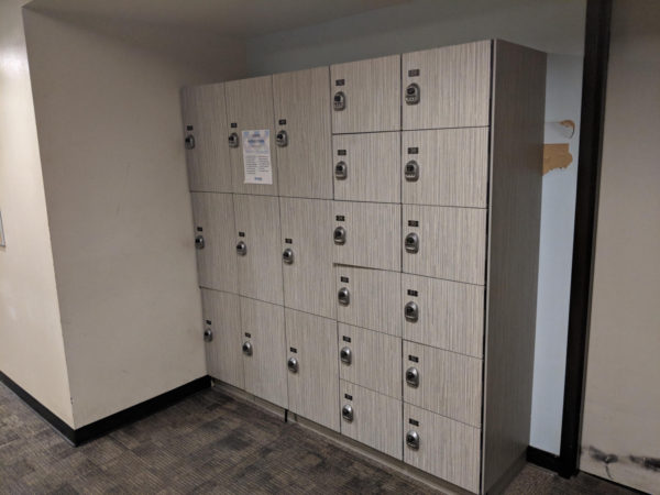 Three-tier and six-tier phenolic lockers in a hallway, with a wood style finish.