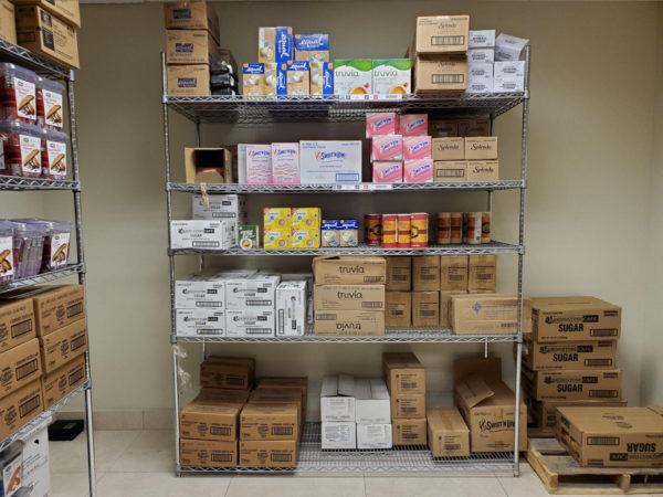 Wire shelving filled with break room items in a storage room.