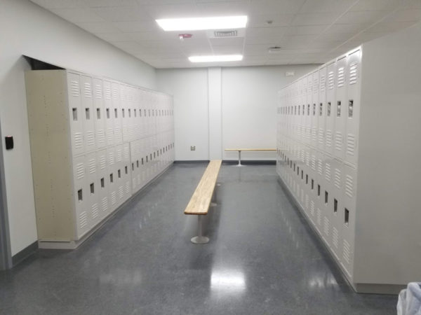 Two-tier standard lockers with an off-white finish and benches in a locker room.